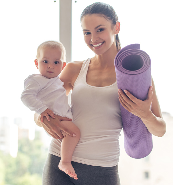 Mama beim Sport mit Baby auf dem Arm und Yogamatte